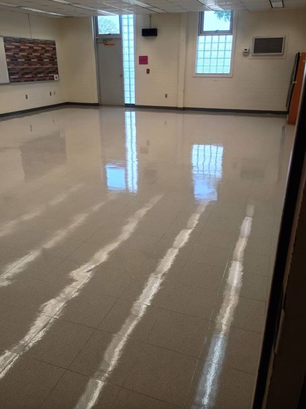 Empty room with shiny, light-colored floor. Windows reflect light, illuminating the space.