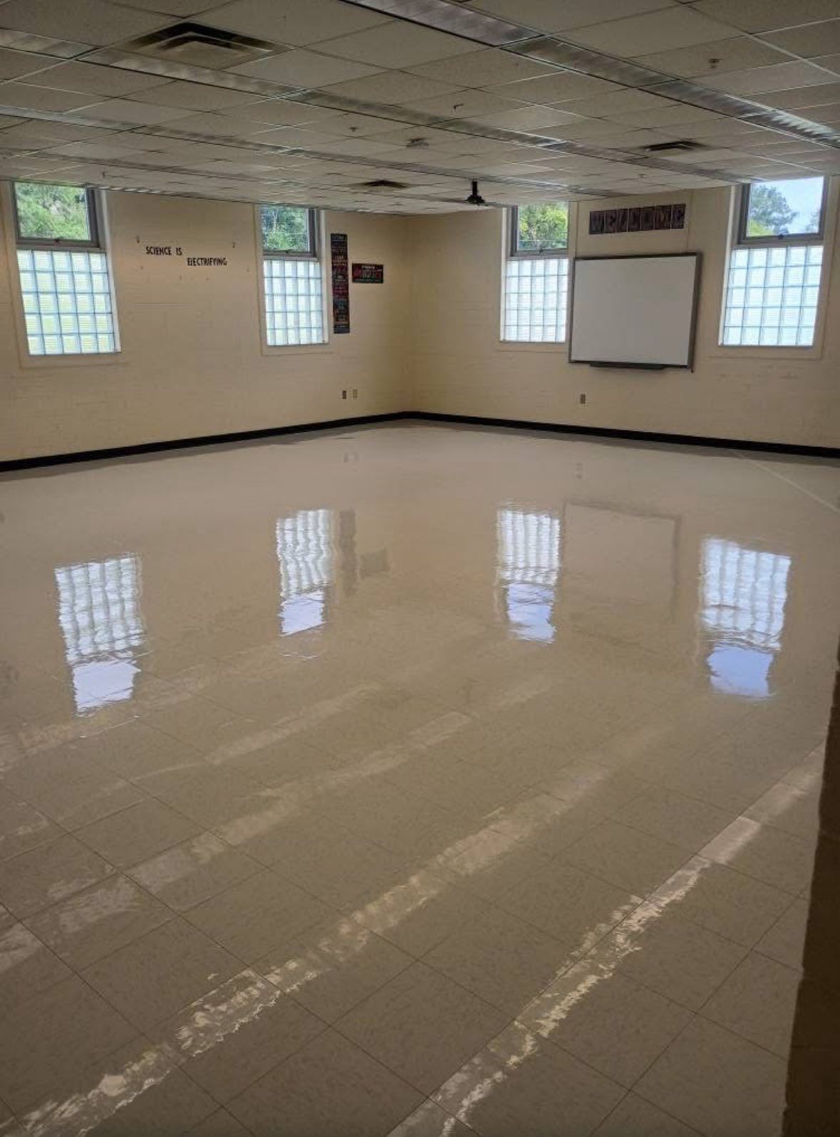 Empty classroom with tiled, glossy floor, windows, and a whiteboard.