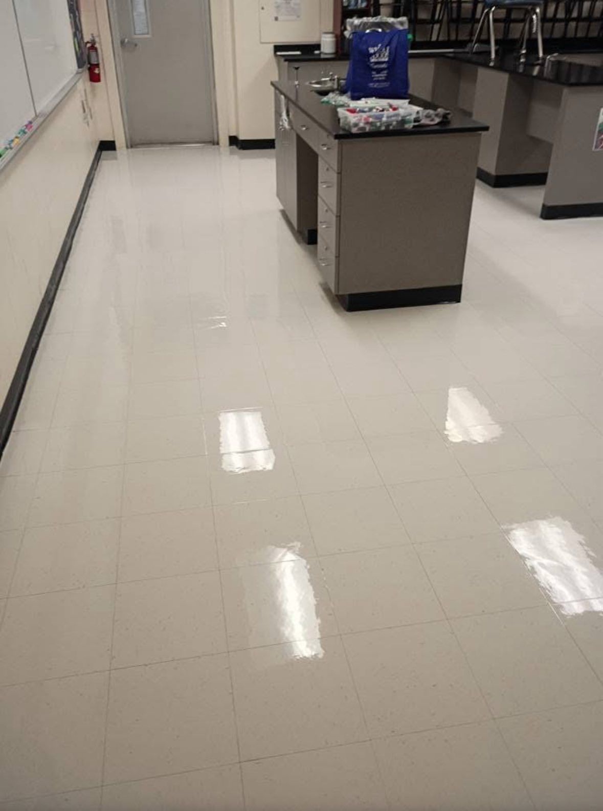 Shiny, light-colored floor in a lab. Gray cabinets and a door are visible in the background.