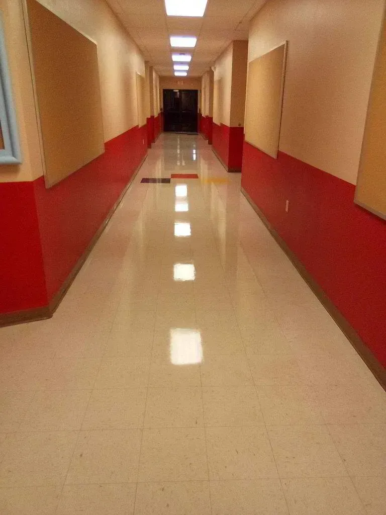 Long hallway with red lower walls, tan upper walls, and bright overhead lights.