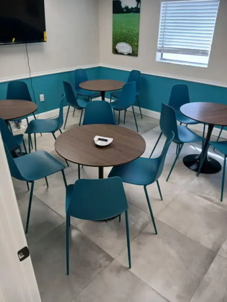 A small room with teal chairs and round brown tables. White and teal walls, gray floor.