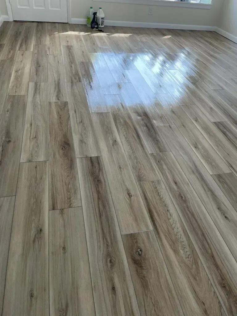 Wooden-look floor with a glossy sheen, reflecting light in a room with a white door.