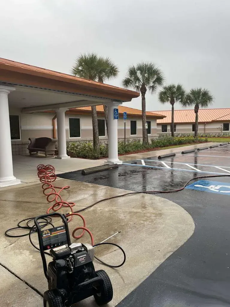 Pressure washer on wet concrete near a building with a tan roof and palm trees.