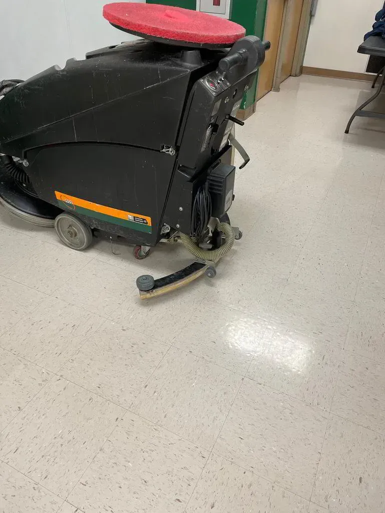 Floor cleaning machine, black and green, with a red pad, cleaning a light-colored floor.