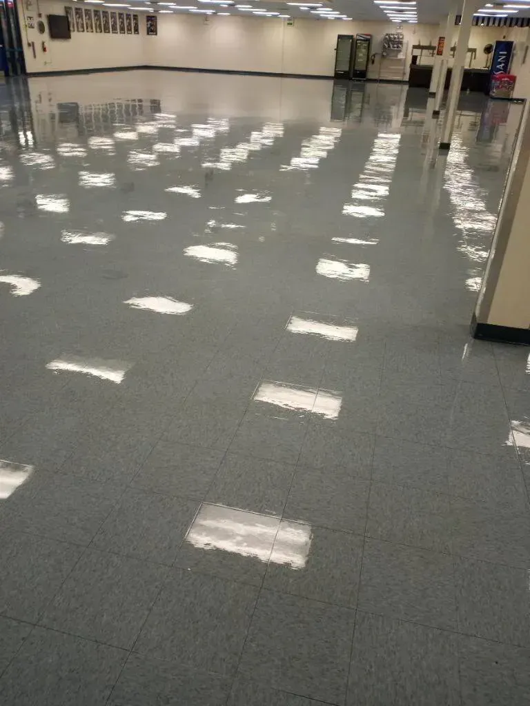 Reflective, gray floor with white rectangles, likely from overhead lights, in a large room.