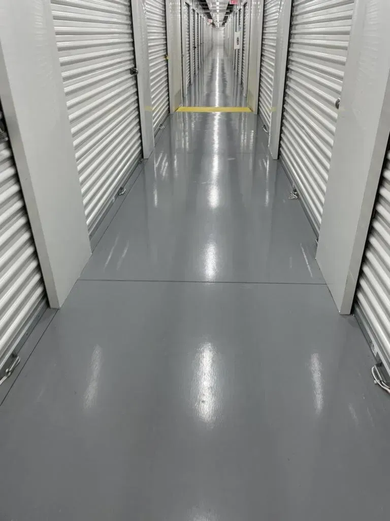 Interior view of a storage unit hallway with shiny gray floor and closed metal doors on both sides.