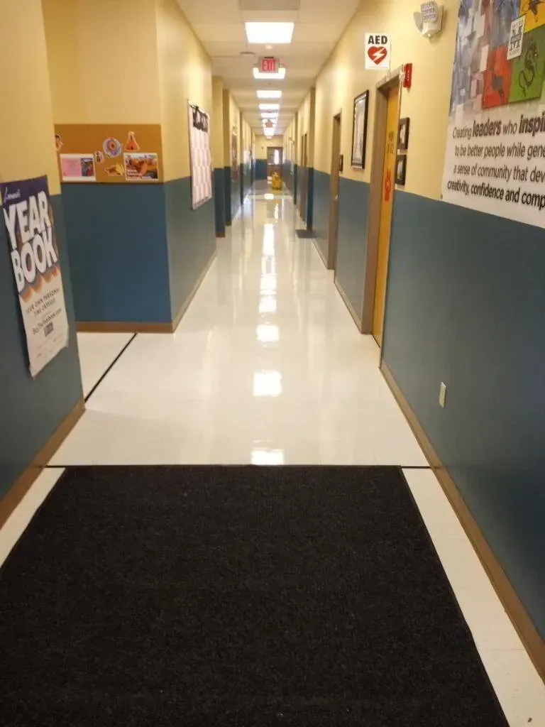 School hallway with blue and yellow walls, a shiny white floor, and several closed doors.