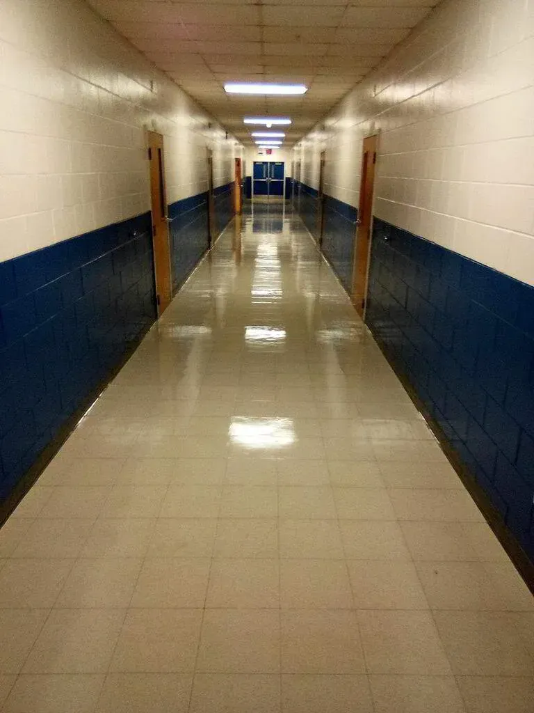 Long, empty school hallway with blue and white walls, and closed wooden doors.