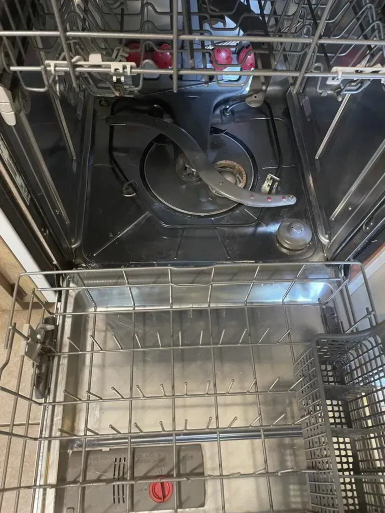 Inside view of a dishwasher, empty with a top rack, water sprayer, and bottom rack.