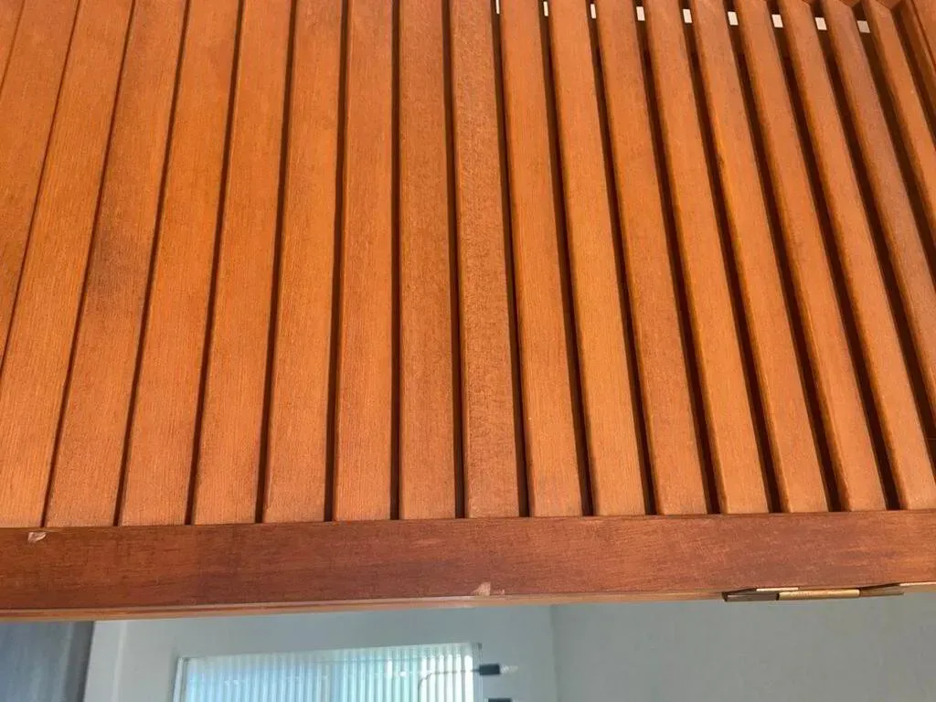 Wooden slatted cabinet door, warm brown hue, partially open, with bright light below.