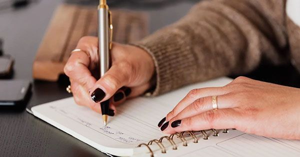 woman's hand holding pen writing in notebook
