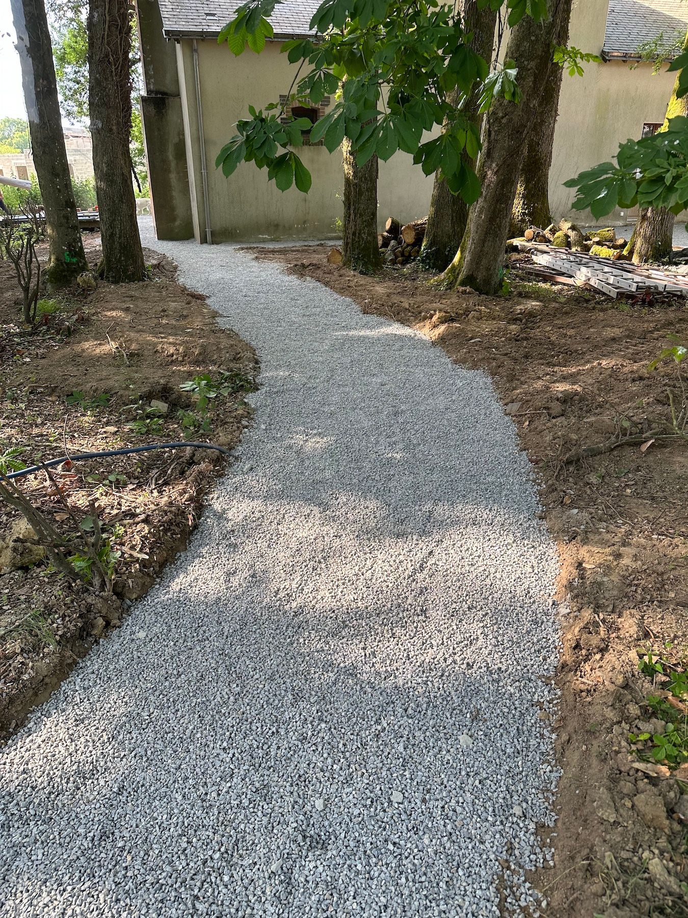 Un chemin de gravier menant à une maison entourée d'arbres.
