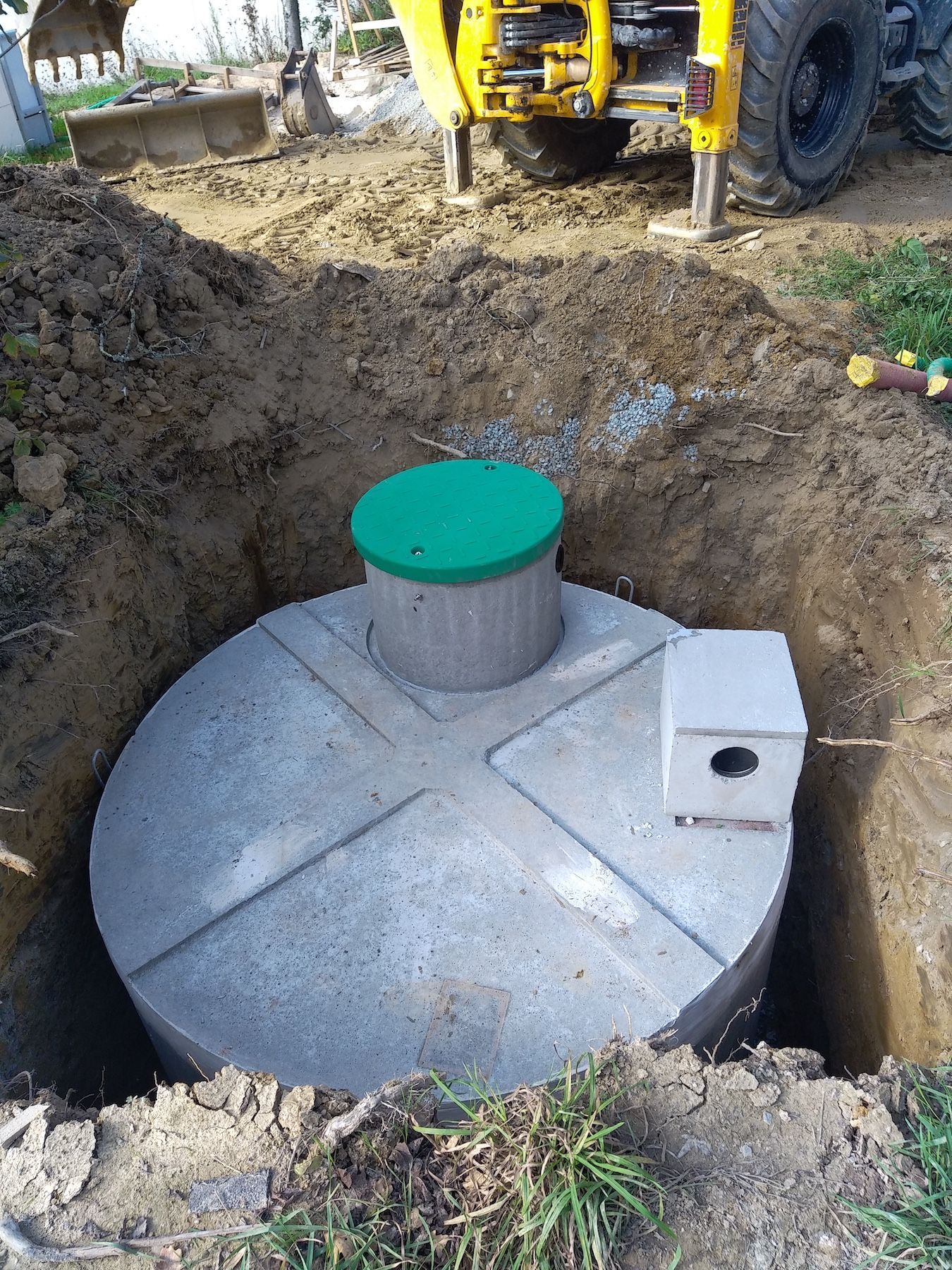 Une fosse septique en béton est en cours d'installation dans un trou dans le sol.