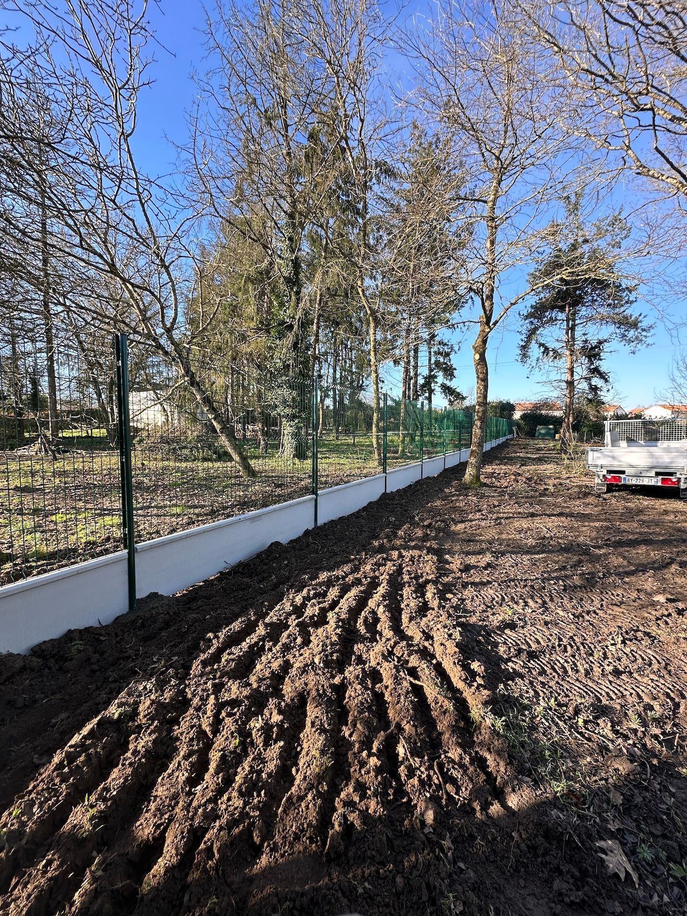 Une clôture blanche entoure un champ de terre avec des arbres en arrière-plan.
