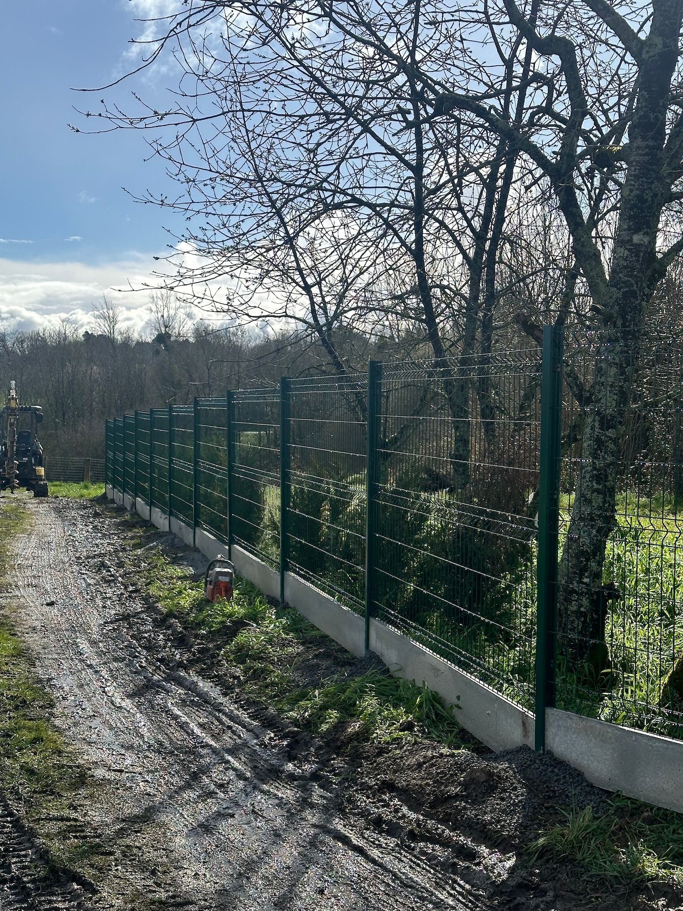 Une clôture est en train d'être construite sur le côté d'un chemin de terre.