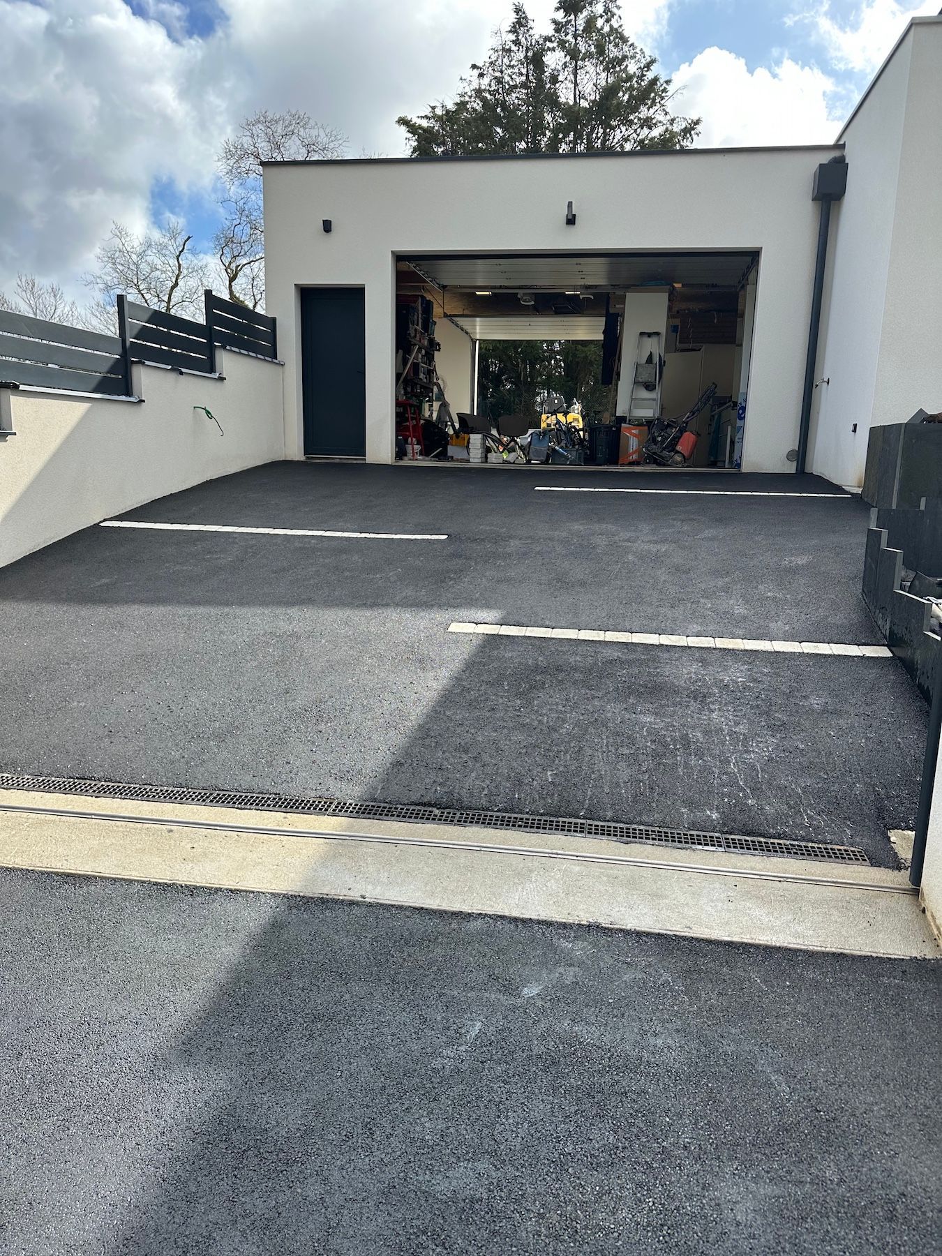 Une allée menant à un garage avec un bâtiment blanc en arrière-plan.