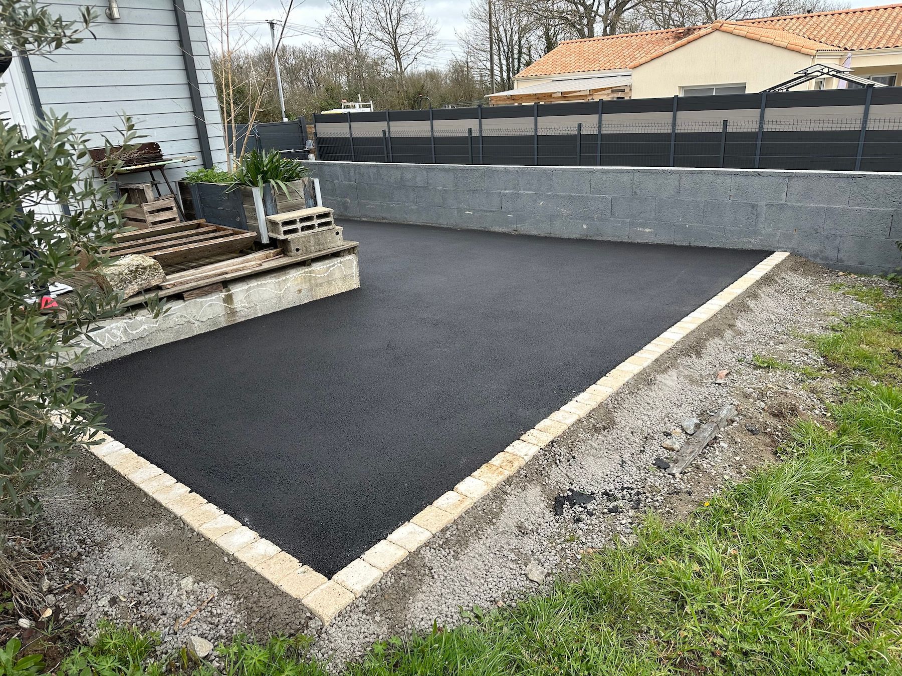 Une allée en asphalte noir avec une bordure blanche et une clôture en arrière-plan.