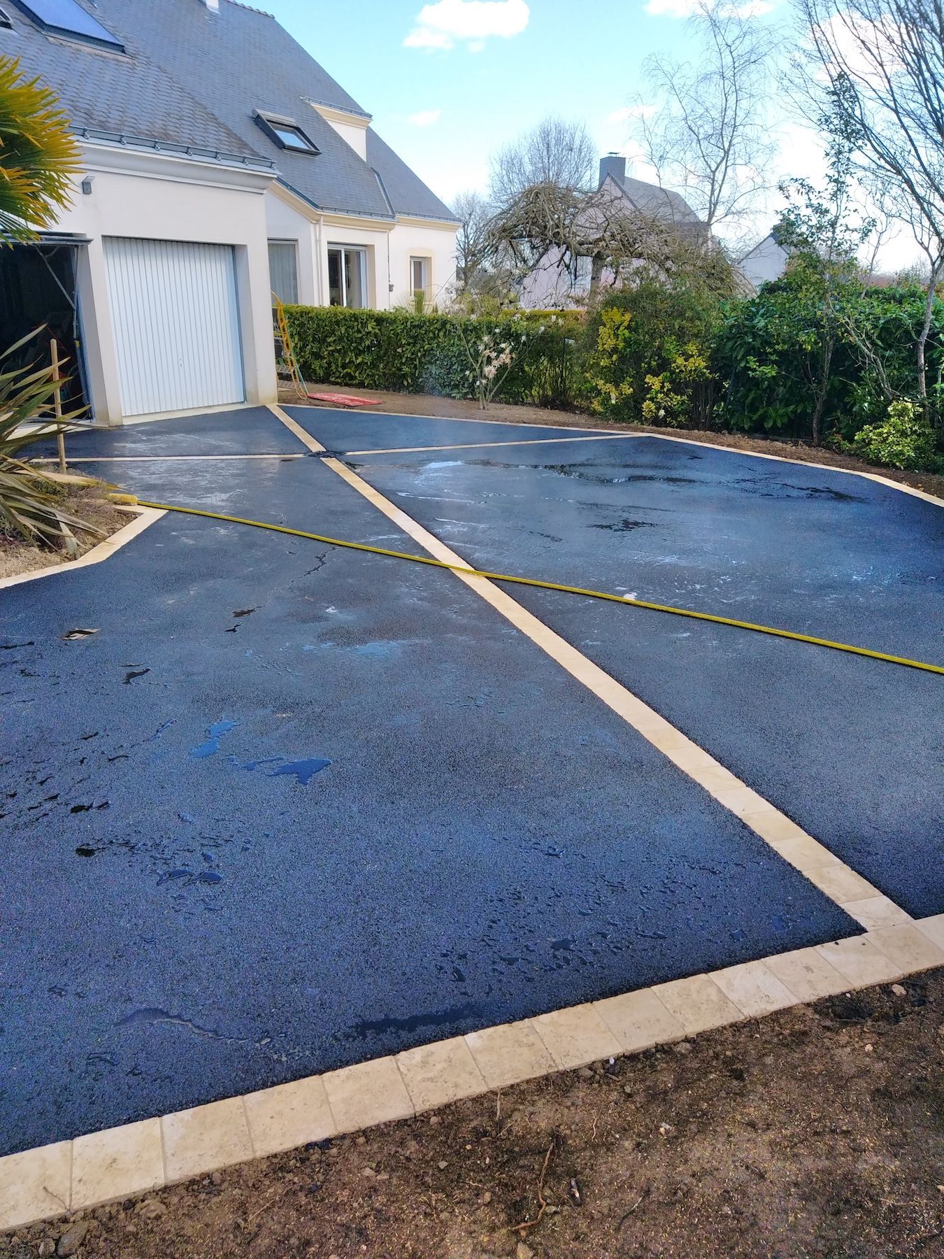 Une allée en asphalte noir avec une ligne blanche devant une maison.