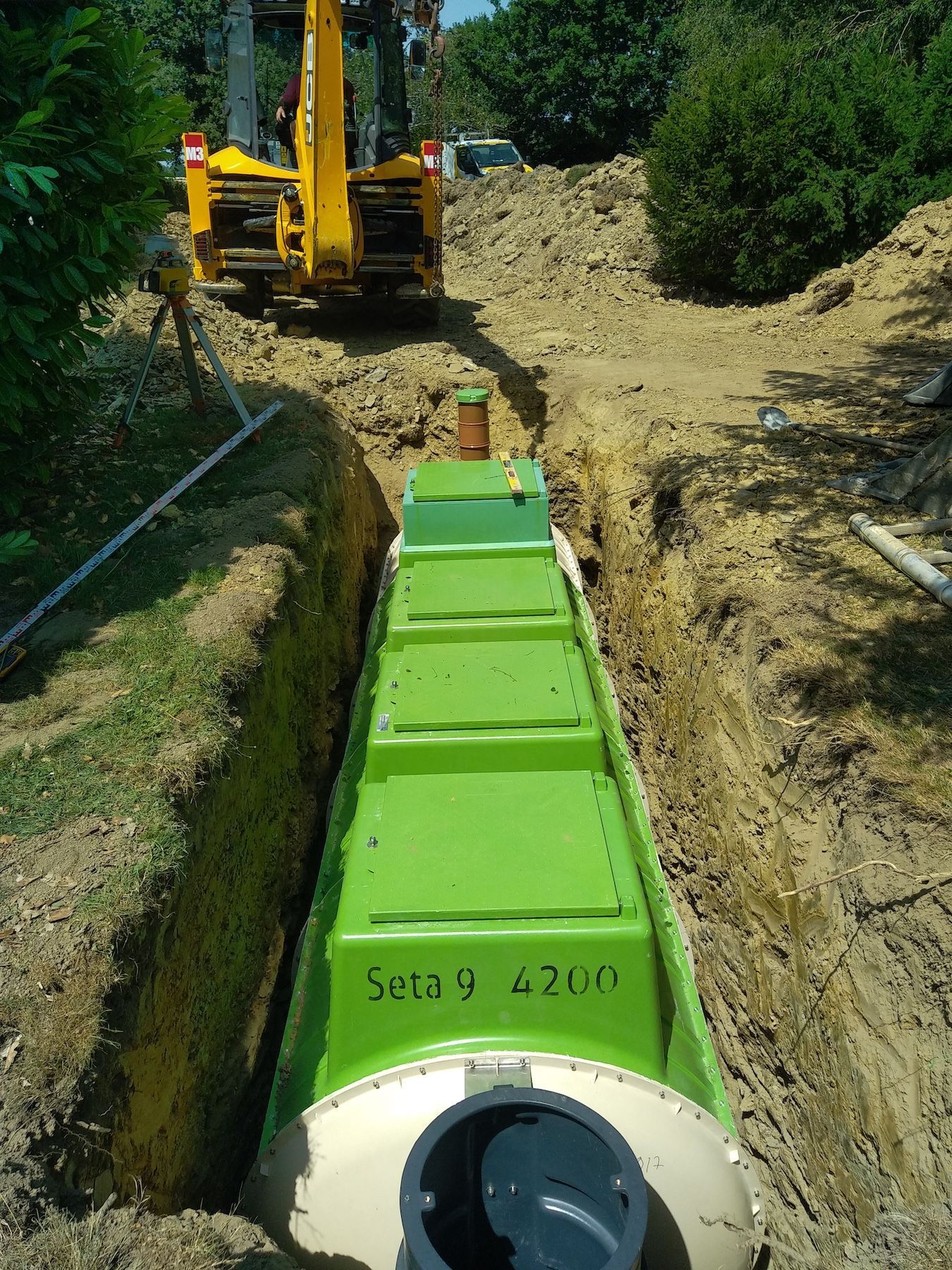 Une fosse septique verte est en cours d'installation dans une tranchée.