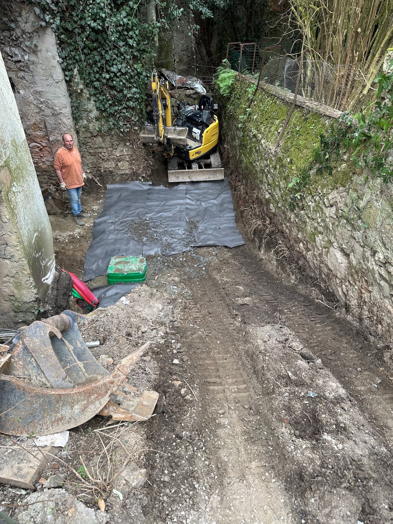 Un homme se tient à côté d'une excavatrice jaune sur un chemin de terre.