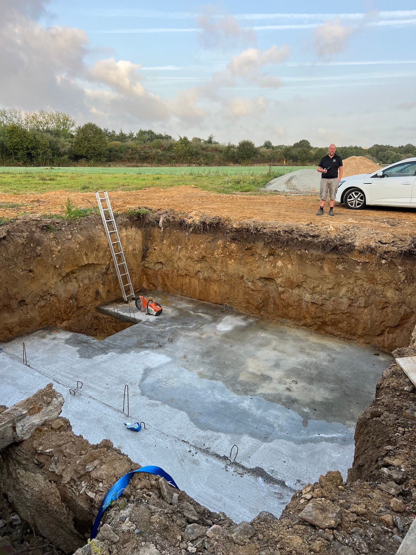 Un homme se tient debout dans un trou dans le sol à côté d'une voiture.