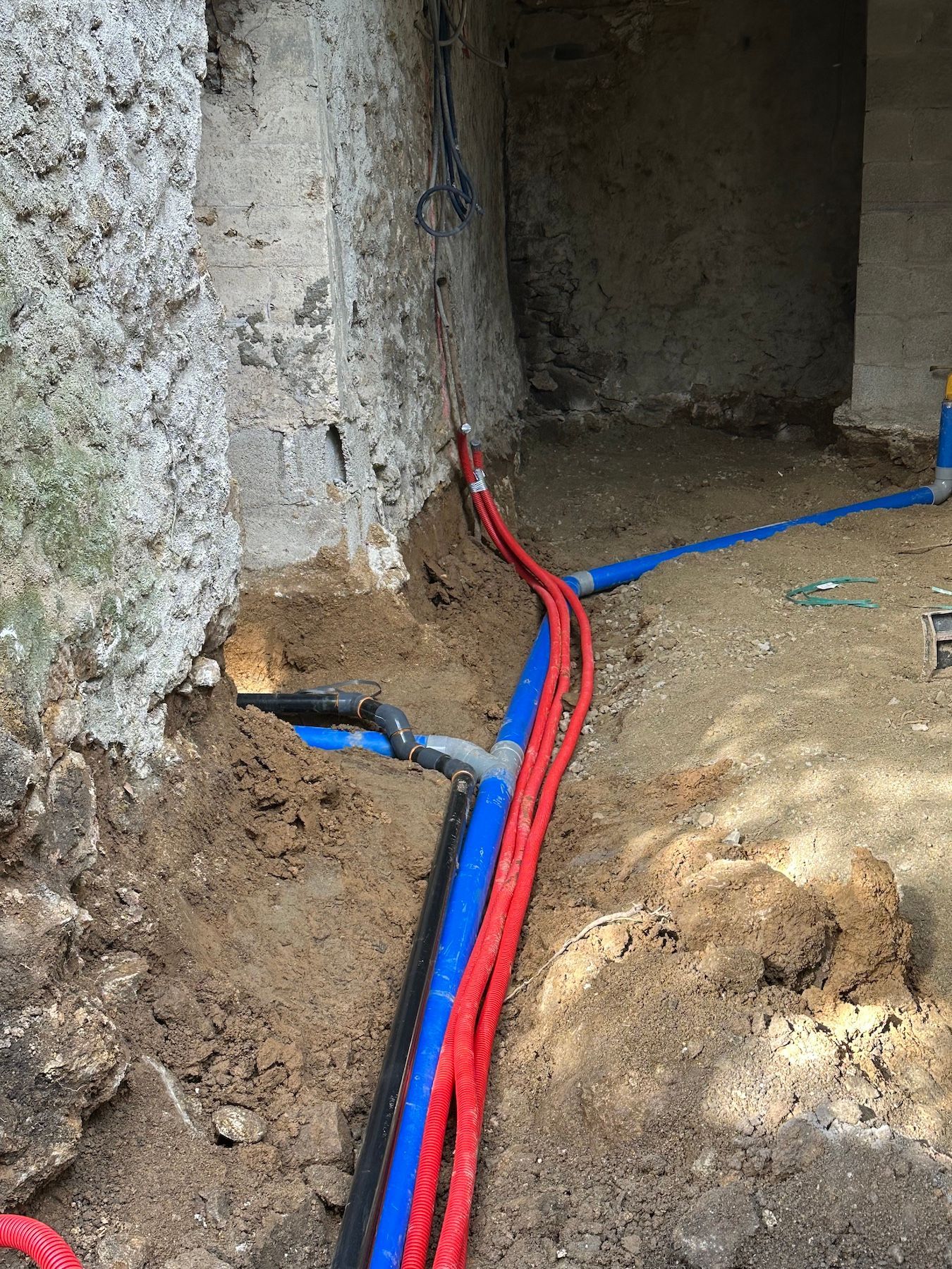 Un tas de fils électriques traînent dans la terre à côté d'un mur.