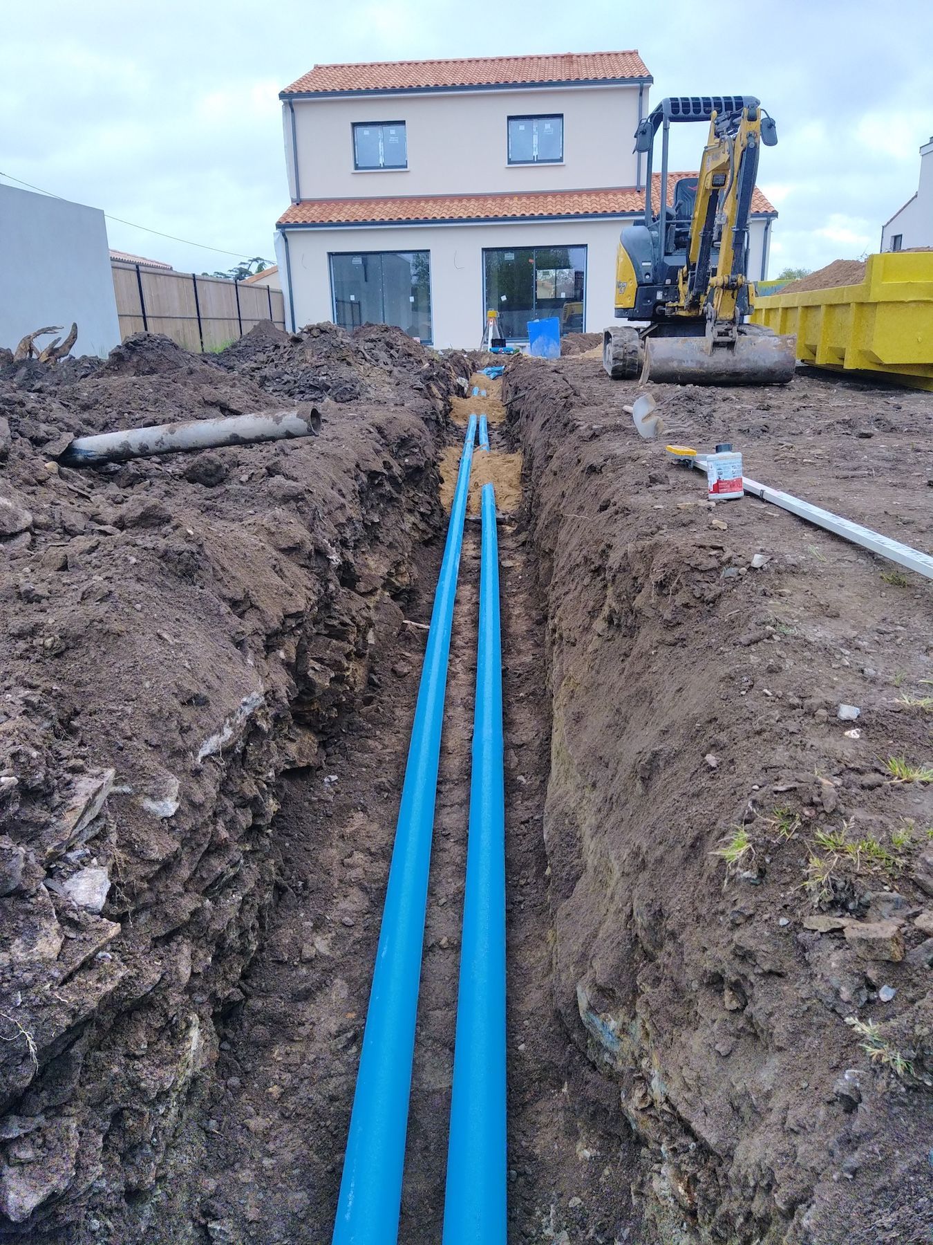 Un tuyau bleu est en train d'être installé dans la terre devant une maison.