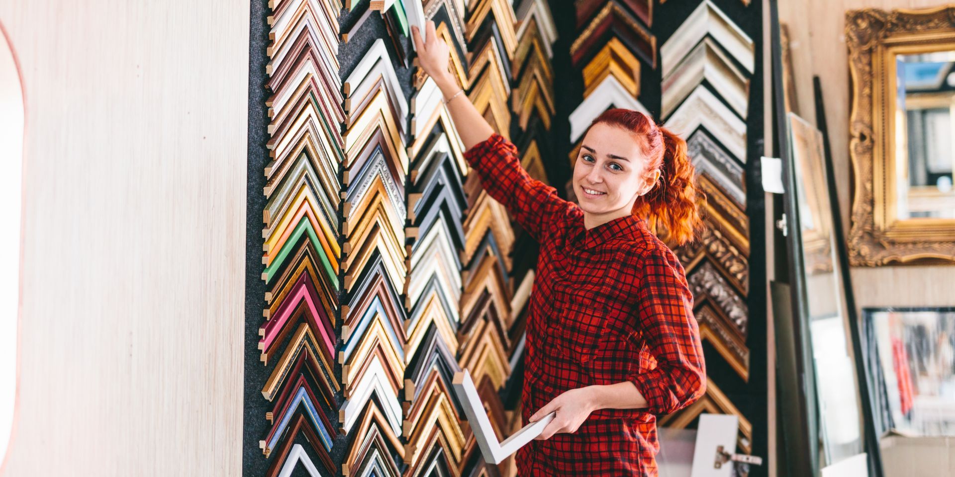 A woman is standing in front of a wall of picture frames.