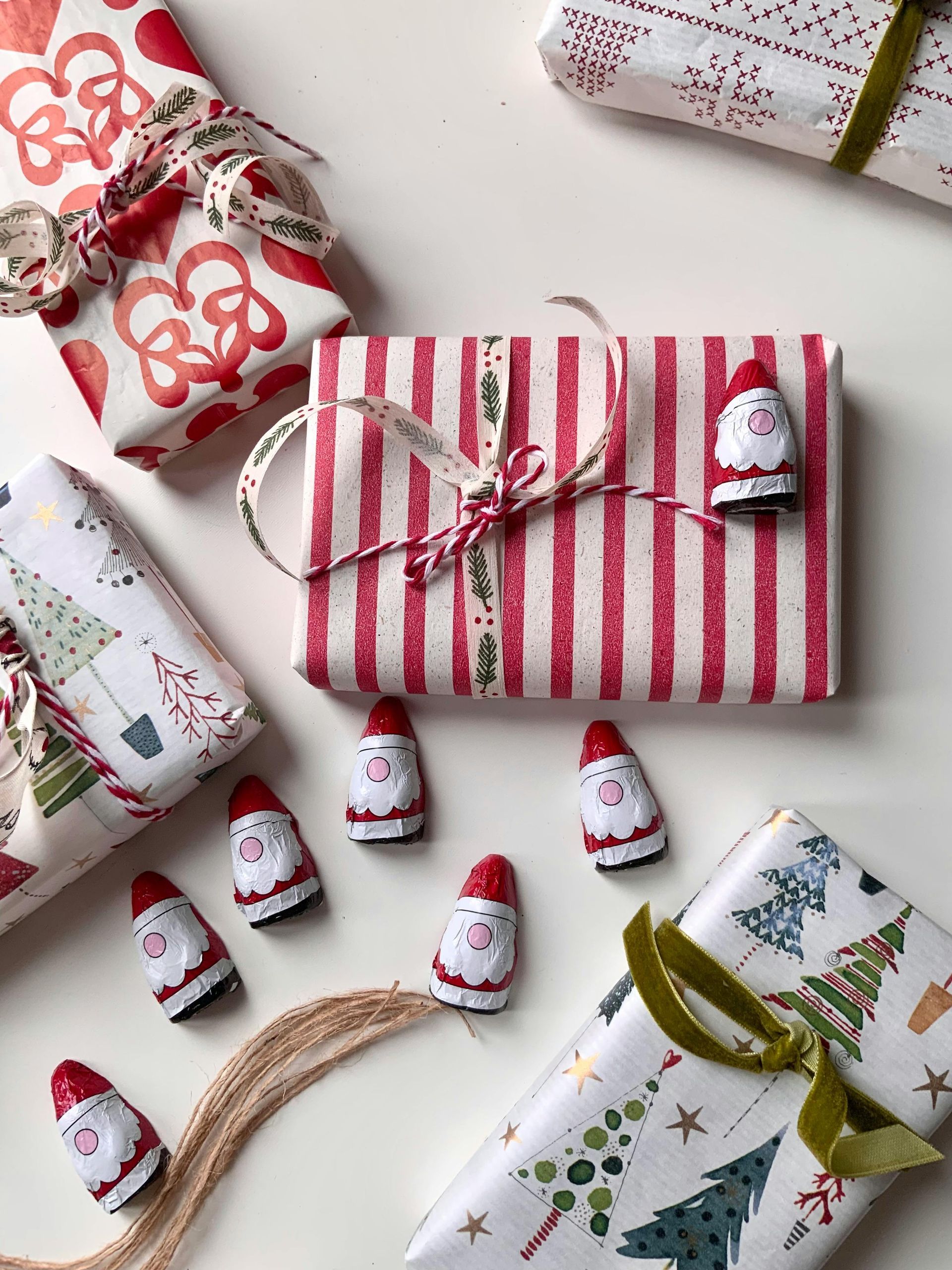 Christmas gifts wrapped in festive paper, decorated with Santa figurines and ribbons on a white surface.