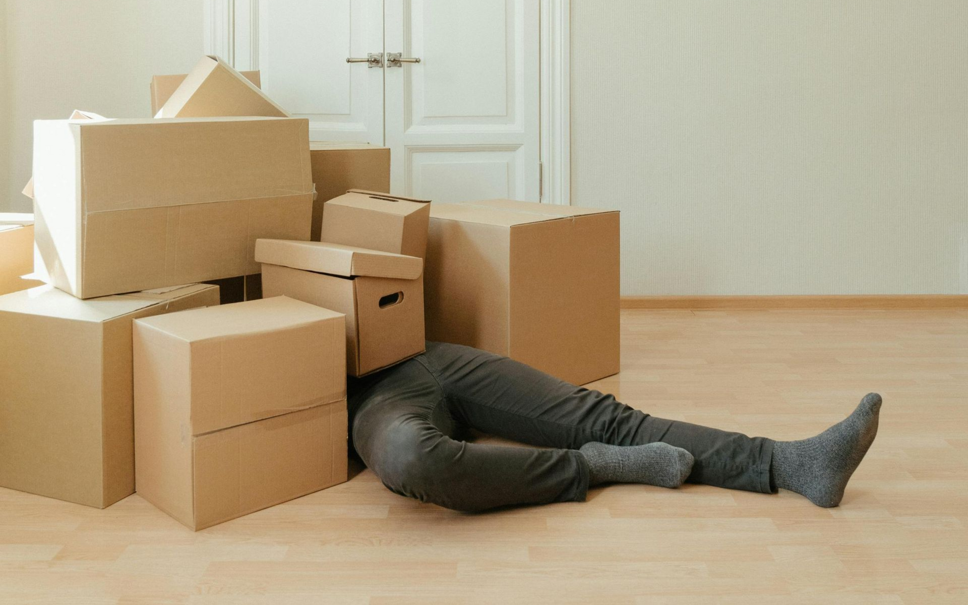 Person sprawled on floor with a box over their head, surrounded by moving boxes in an empty room.