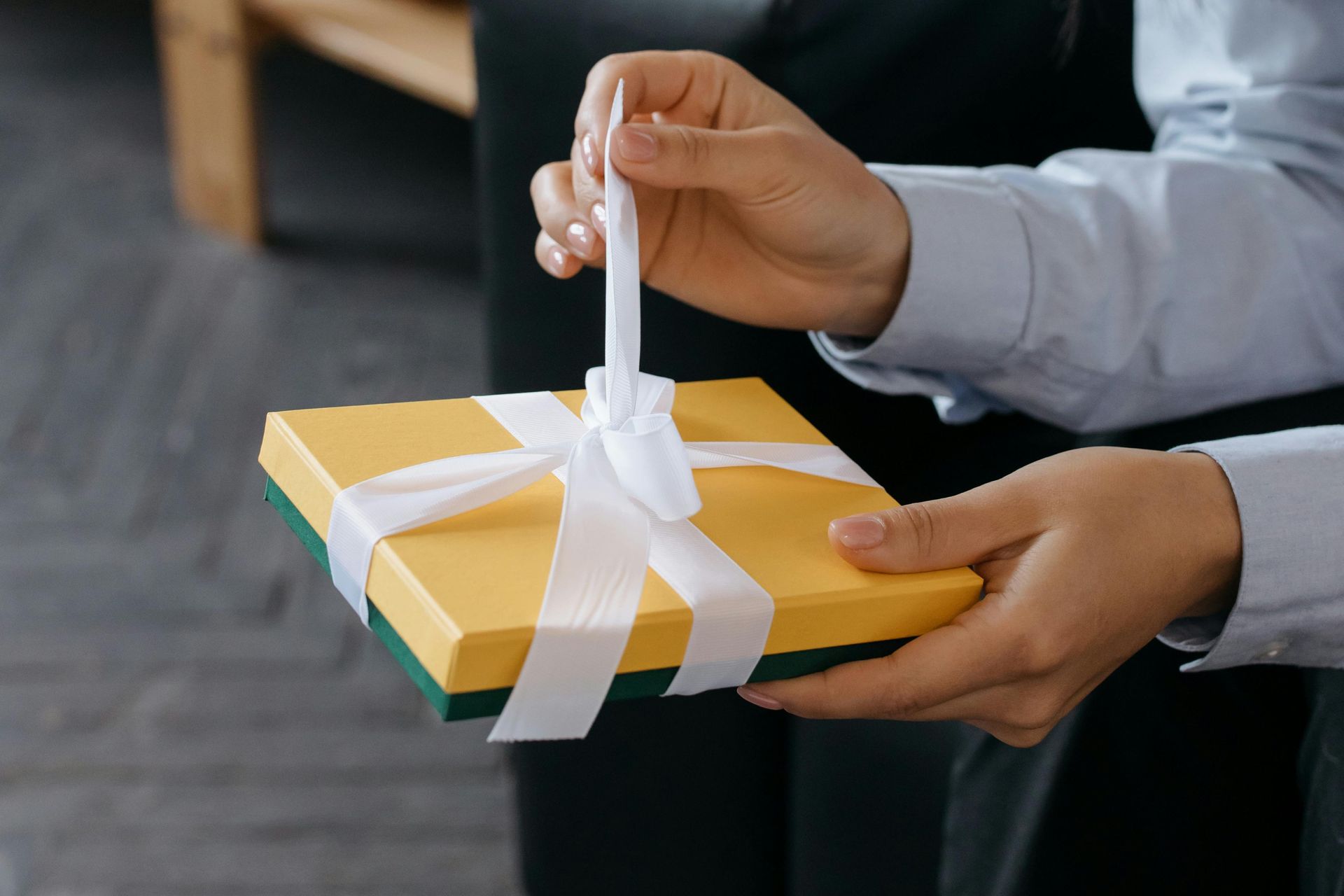 Person in blue shirt opening a yellow gift box tied with white ribbon.