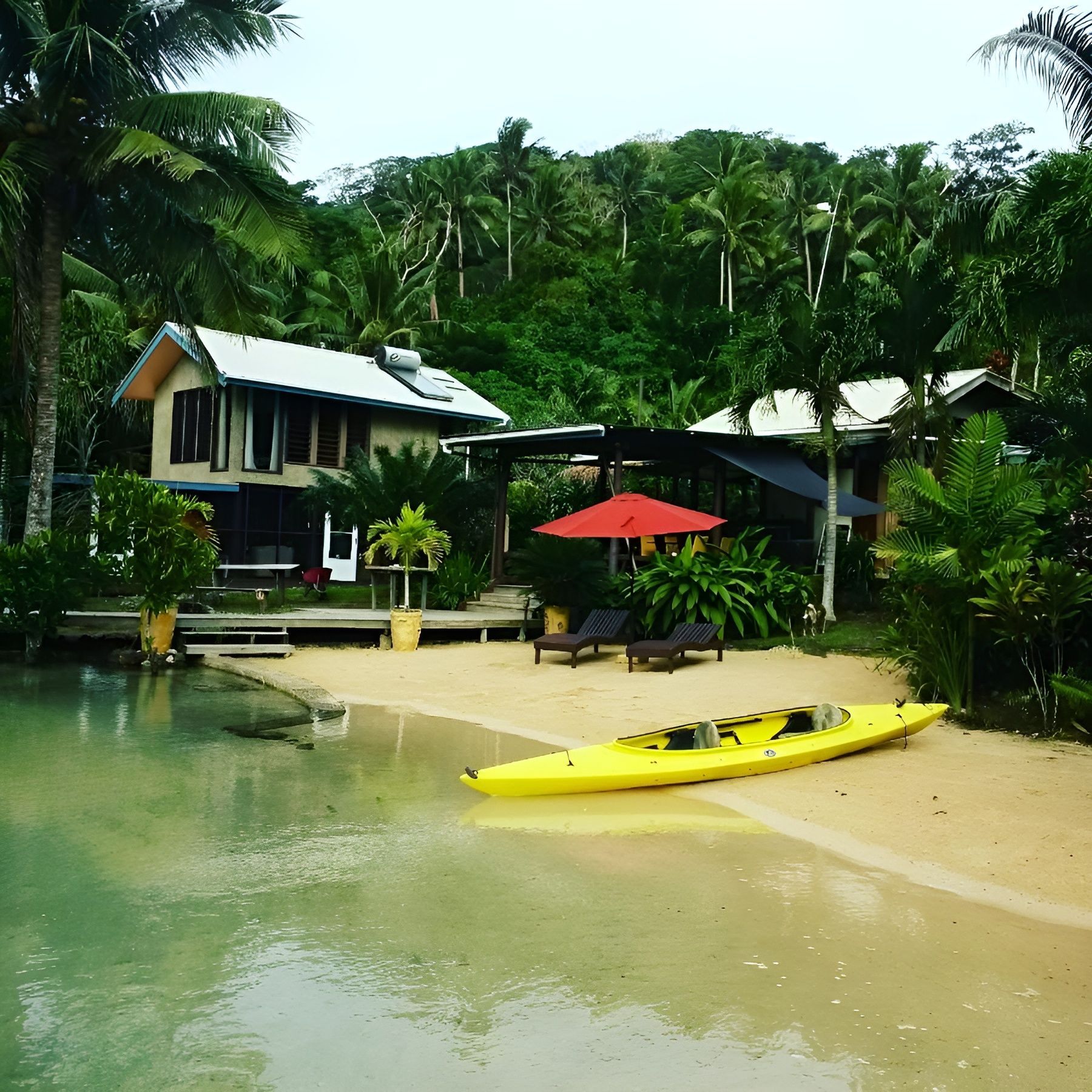 A yellow kayak sits on a sandy beach in front of a house