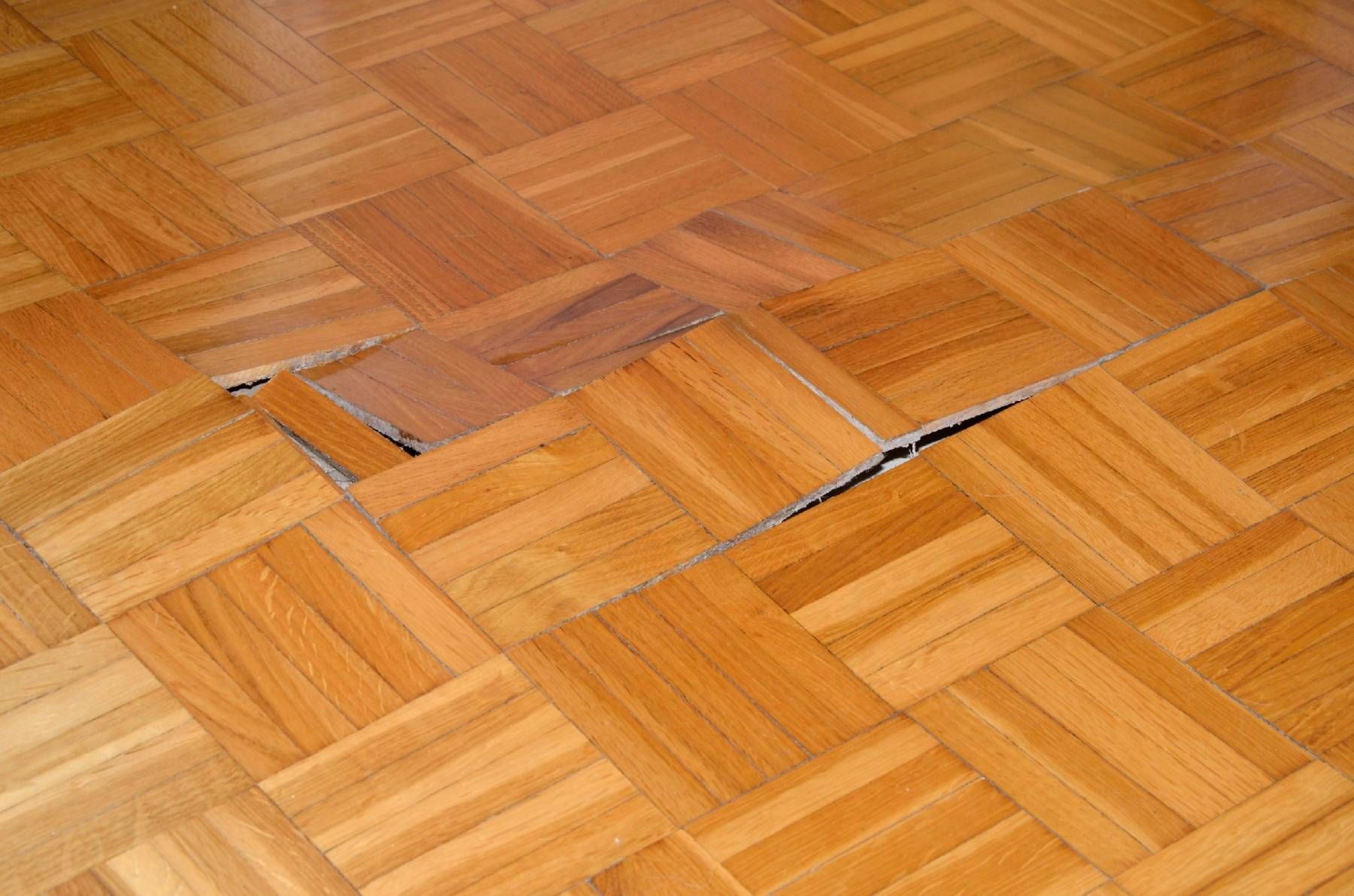 Damaged parquet flooring with a gap exposing the subfloor.