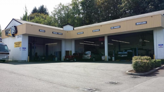 Exterior view of an auto repair shop with open garage bays, beige trim, and vehicles inside.