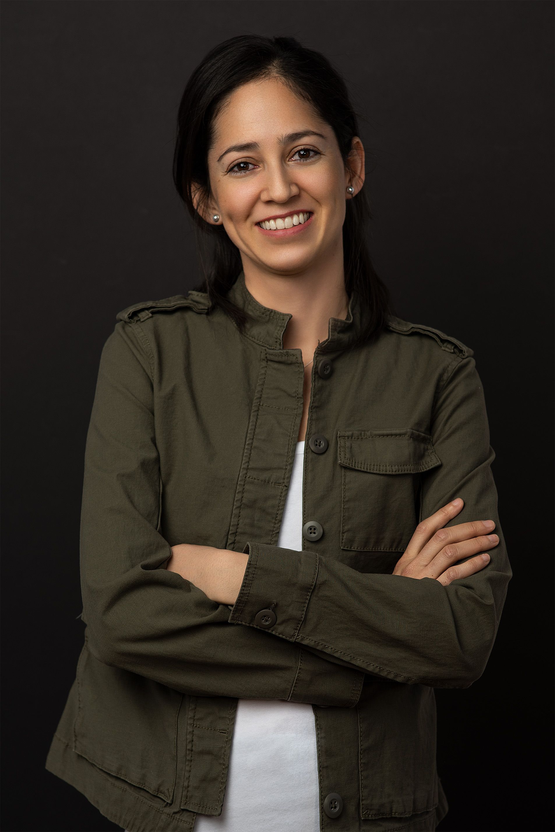 A woman in a green jacket is standing with her arms crossed and smiling.