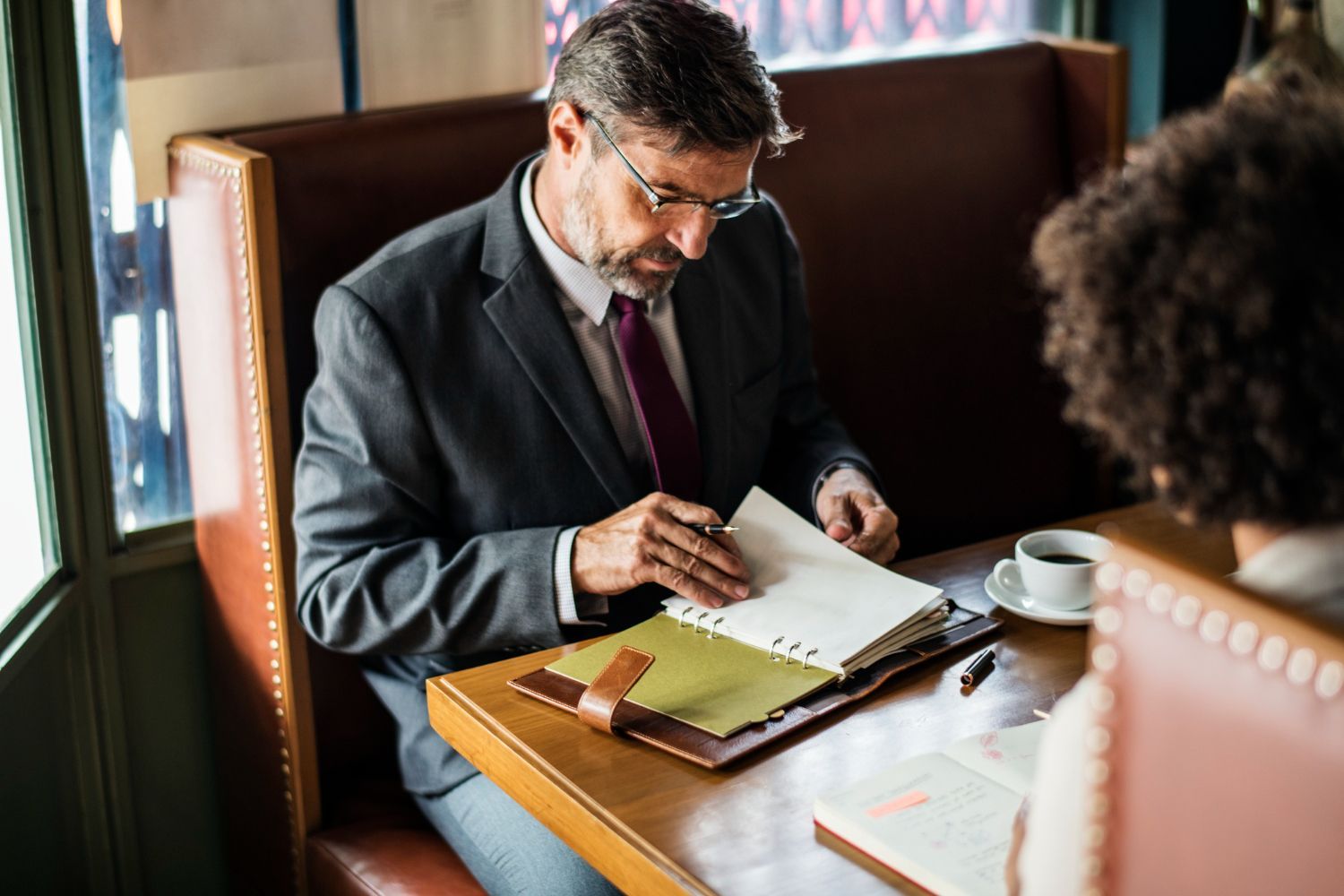 Man and woman at table in a restaurant, holding hands. Woman in suit reads from a notebook.