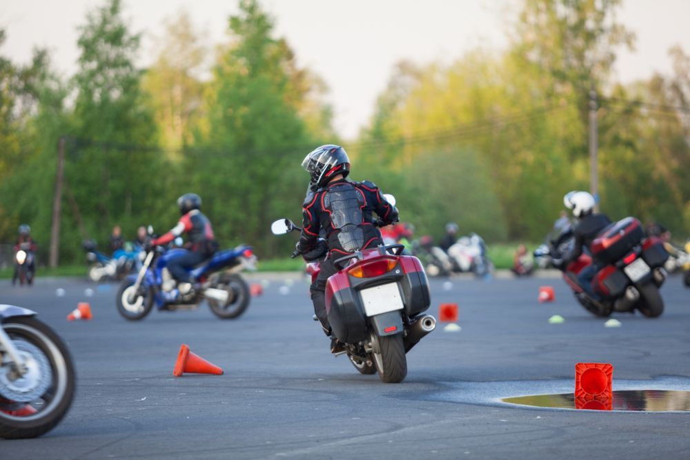 Motorcycle riders practicing maneuvers on a course marked with cones.