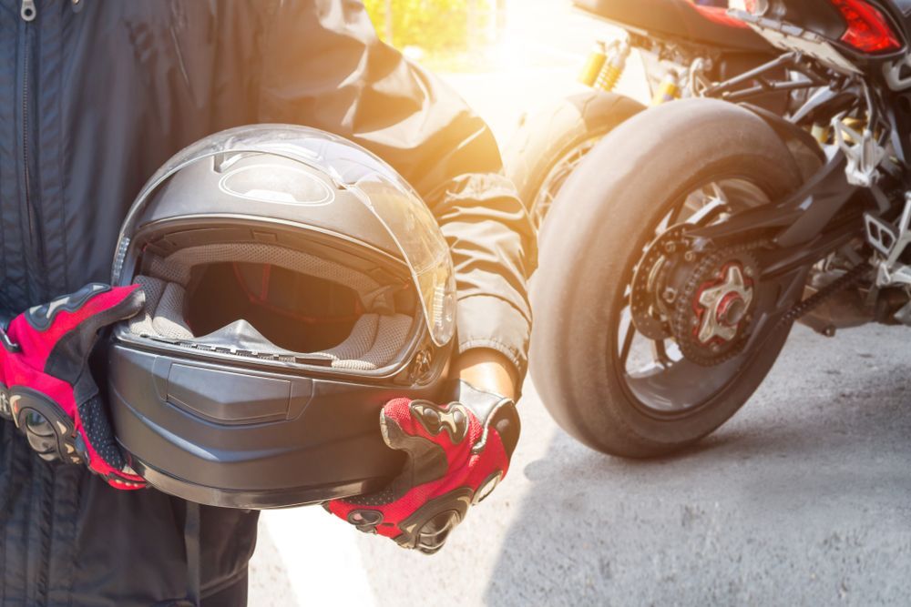 Person holding a black motorcycle helmet near a motorcycle, wearing gloves.