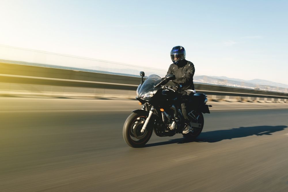 Motorcyclist in black riding on a highway under a clear sky.