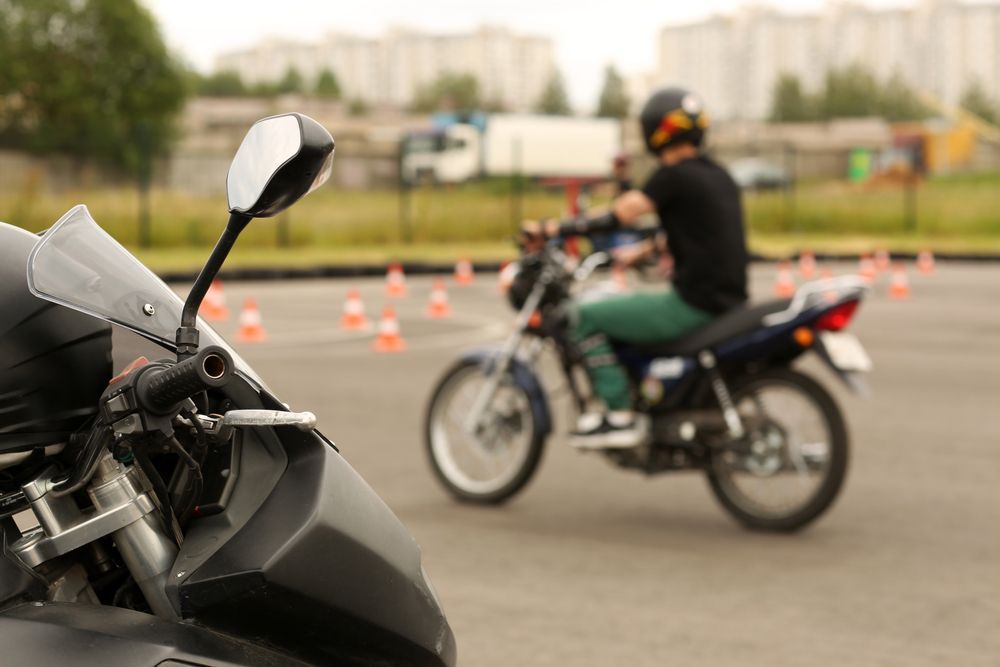 Motorcycle training: rider on a blue bike, practicing maneuvers with cones in a paved area.