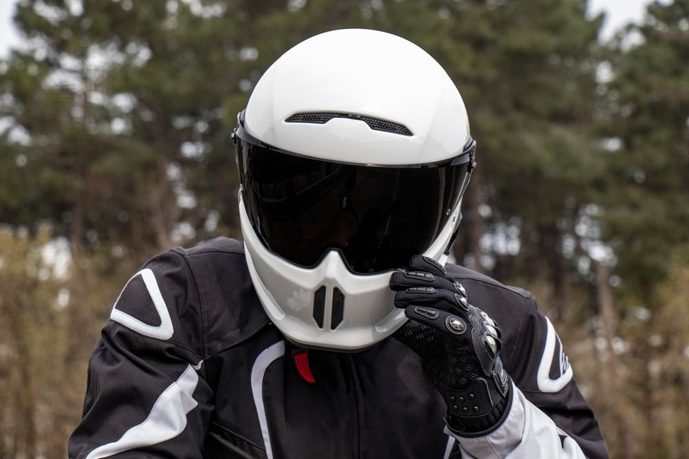 Person wearing a white motorcycle helmet with a tinted visor, adjusting their gear outdoors.
