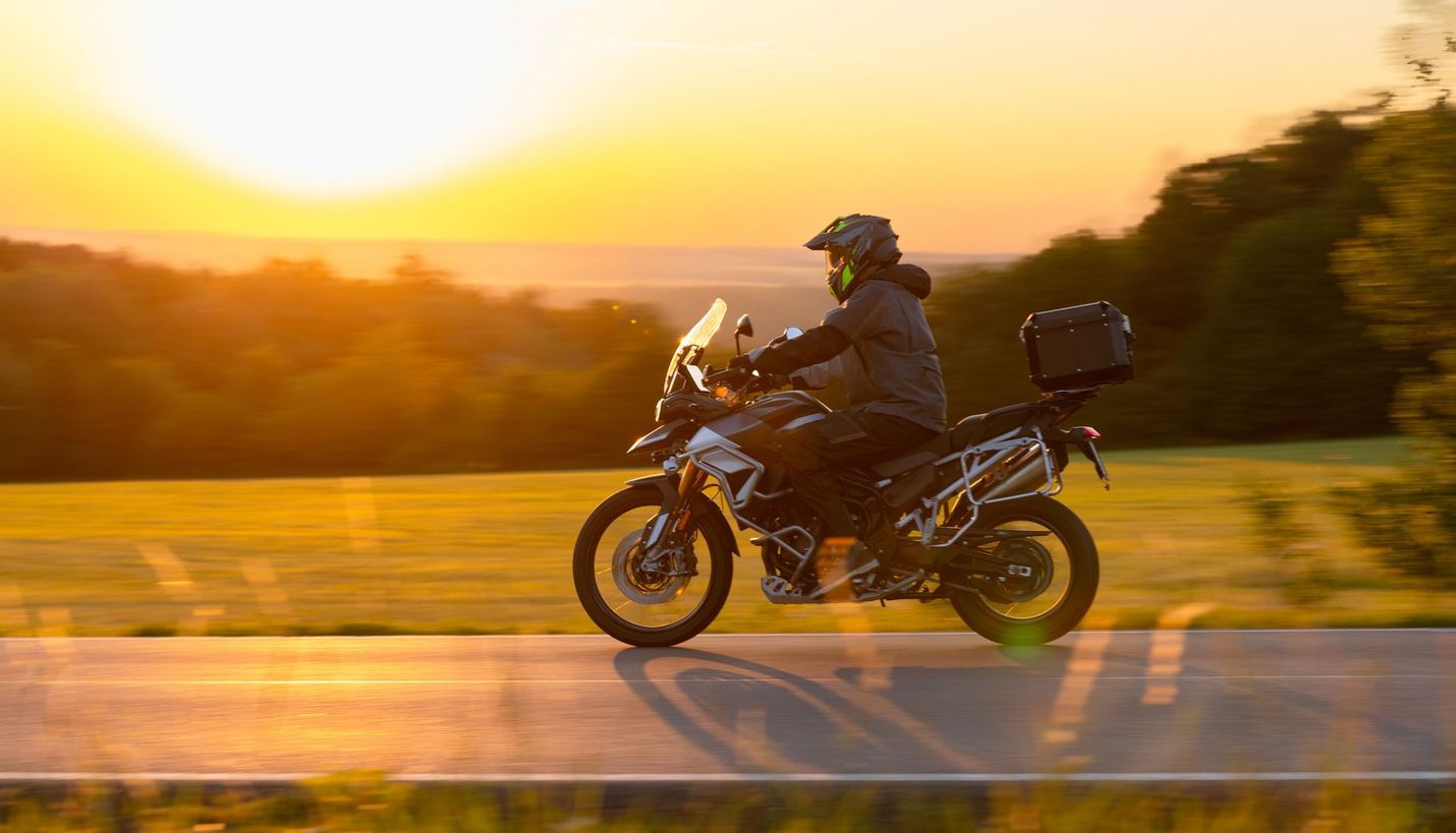 Motorcyclist rides a motorcycle down a road at sunset.