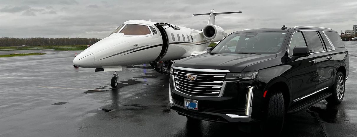 A black suv is parked next to a private jet on a wet runway.