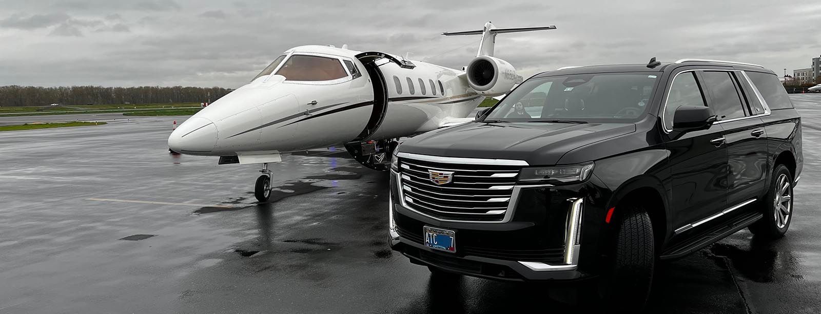 A black suv is parked next to a private jet on a wet runway.