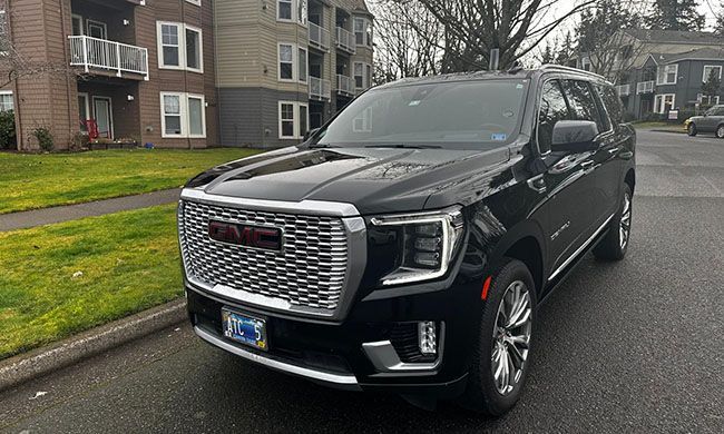 A black gmc yukon is parked on the side of the road in front of a apartment building.