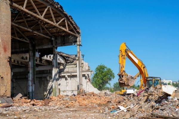 A yellow excavator is demolishing an old building.