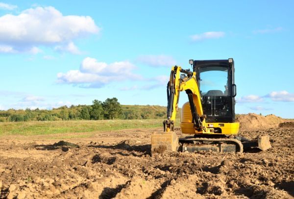 A yellow excavator is digging a hole in a dirt field.