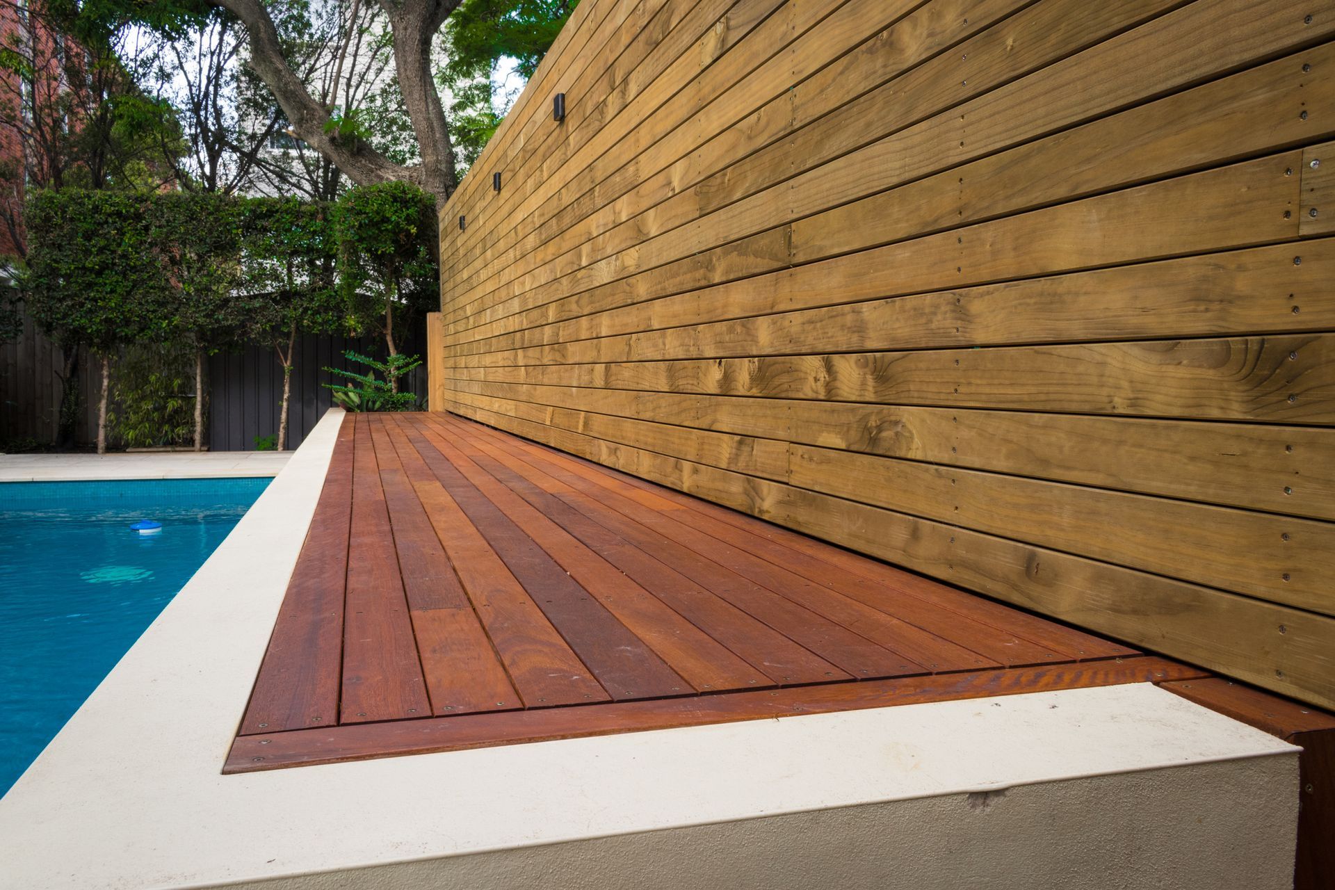 A wooden deck sits next to a swimming pool.