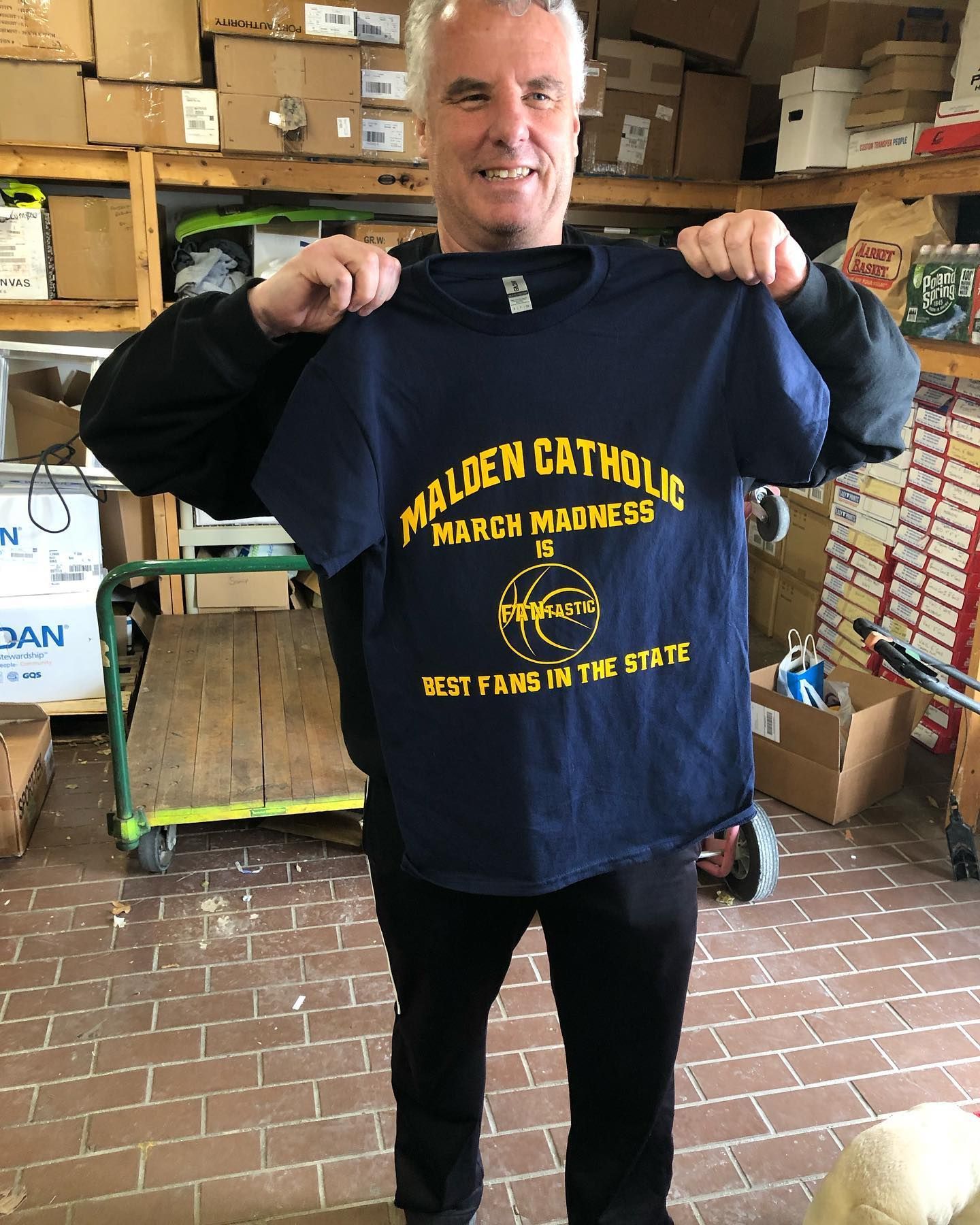 Man holding a navy blue Malden Catholic t-shirt with gold lettering.