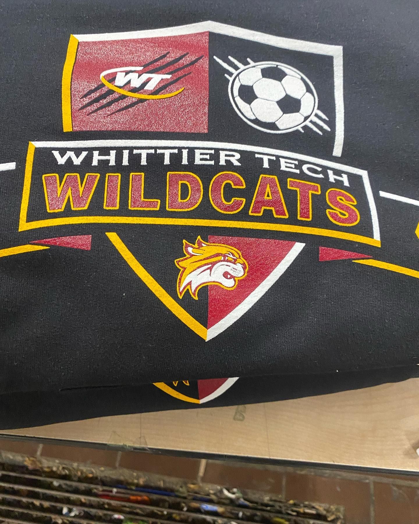 Whittier Tech Wildcats logo on black fabric, with red, gold, and white elements, including a soccer ball and wildcat graphic.